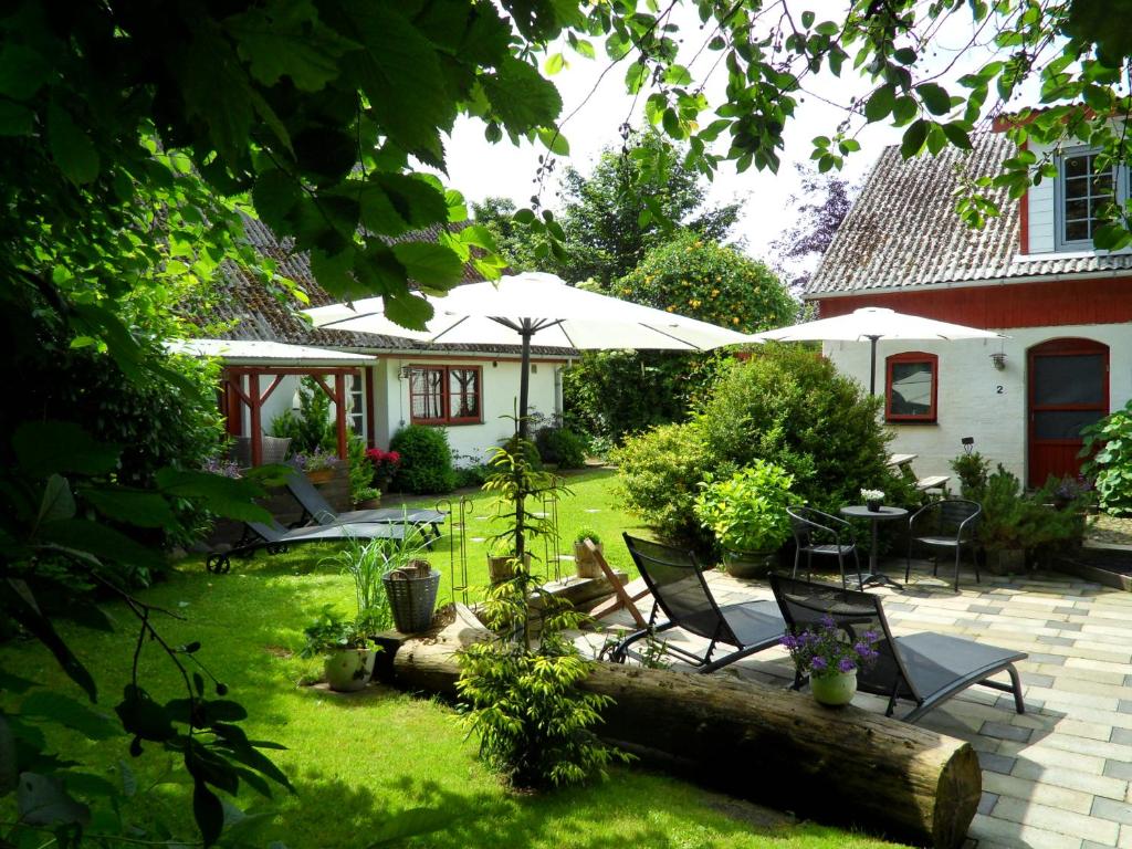 einen Garten mit Stühlen, Tischen und einem Sonnenschirm in der Unterkunft Lille Degnbøl Holiday House in Degnbøl