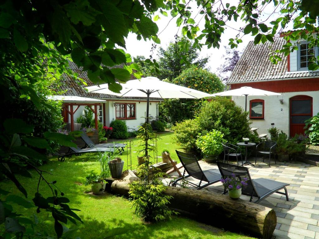 un jardín con sillas, mesas y sombrilla en Lille Degnbøl Holiday House, en Degnbøl