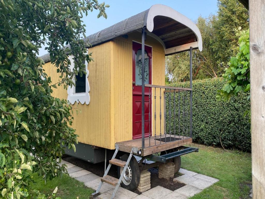 a yellow house with a red door in a yard at Gypsy Caravan in Weideblick with Farm Animals in Bergen op Zoom