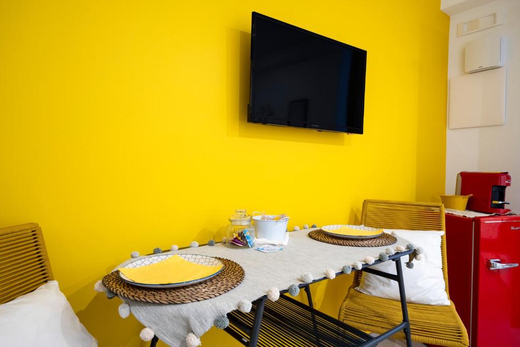 ein Tisch mit zwei Stühlen und einem Fernseher an einer gelben Wand in der Unterkunft Dimora dei Colori - Yellow Light in Bari