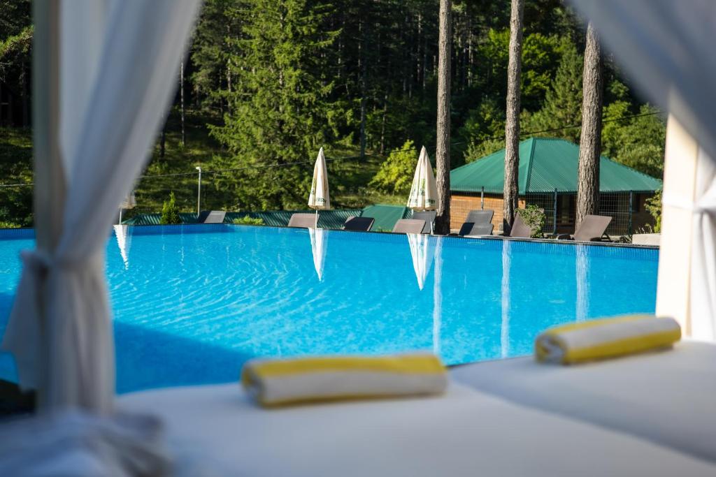 a blue swimming pool with chairs and umbrellas at Vila Sunce Village Resort Konjic in Konjic