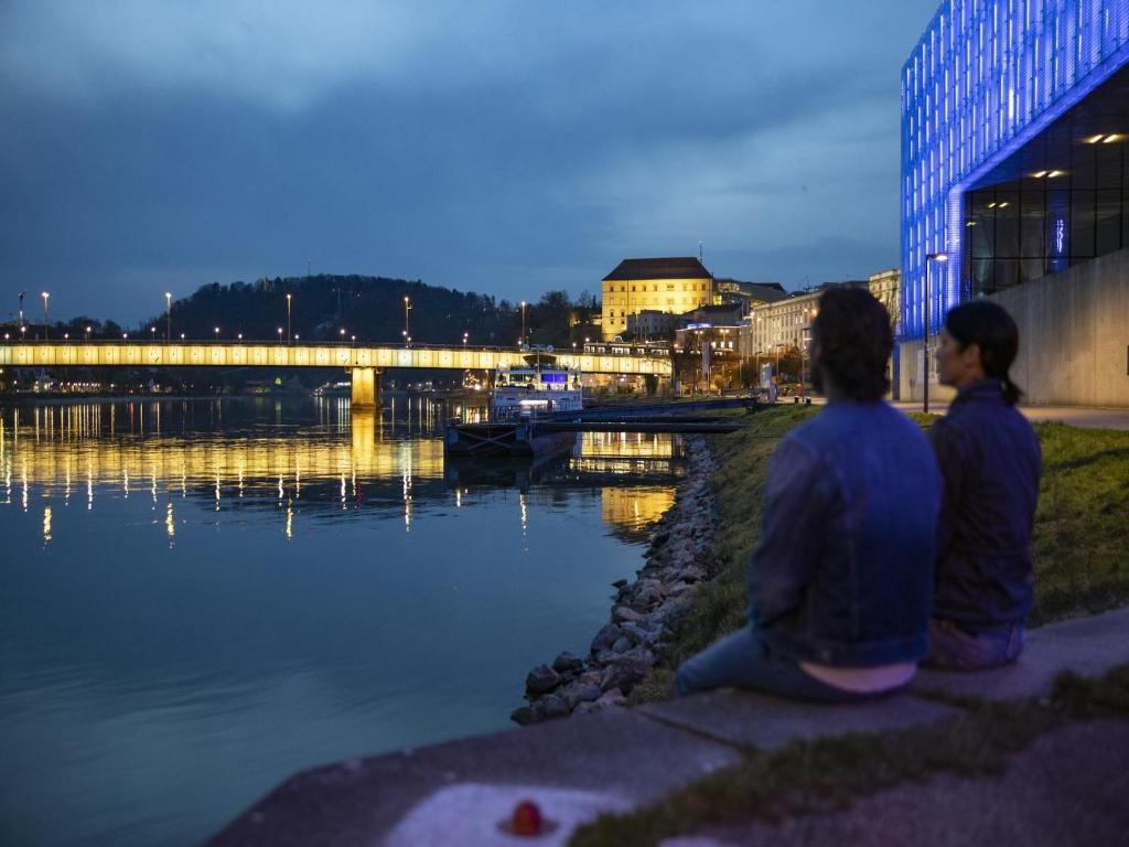 Dos personas sentadas junto a un río por la noche. en Appartements nicht weit von der Donau, en Linz