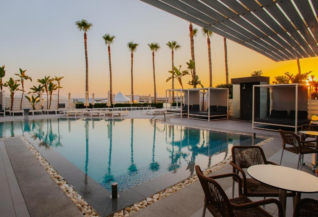 a swimming pool with tables and chairs and palm trees at Tasia Maris Sands (Adults Only) in Ayia Napa