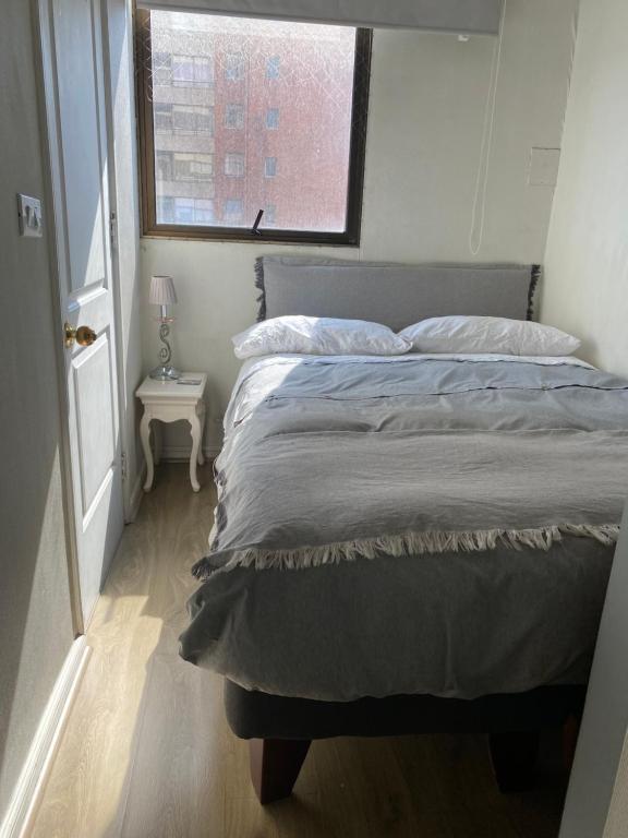 Una cama en una habitación pequeña con ventana. en Habitación Metro Escuela Militar, en Santiago