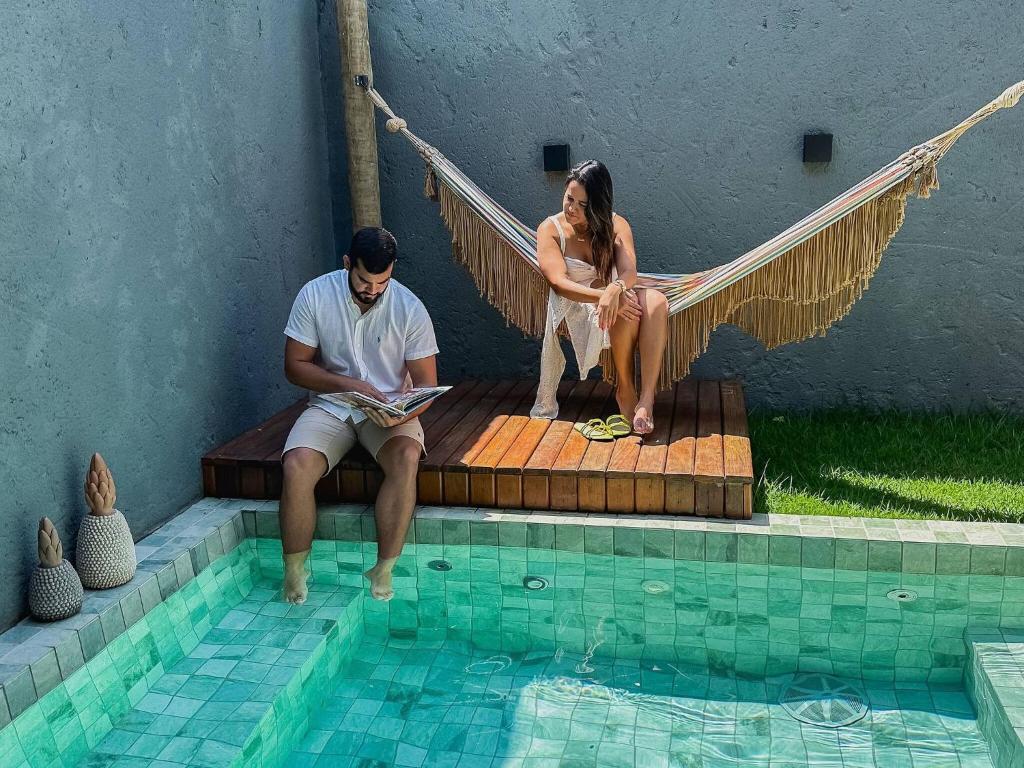 un homme et une femme assis dans un hamac au bord d'une piscine dans l'établissement Pousada Nori - Por MME Hospitalidade, à São Miguel dos Milagres