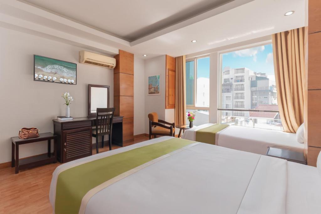 Una habitación de hotel con dos camas, un escritorio y una ventana. en Ola Hotel & Apartment, en Nha Trang