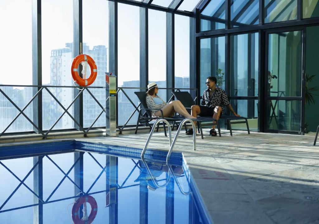 two people sitting on chairs next to a swimming pool at Radisson Oscar Freire in São Paulo