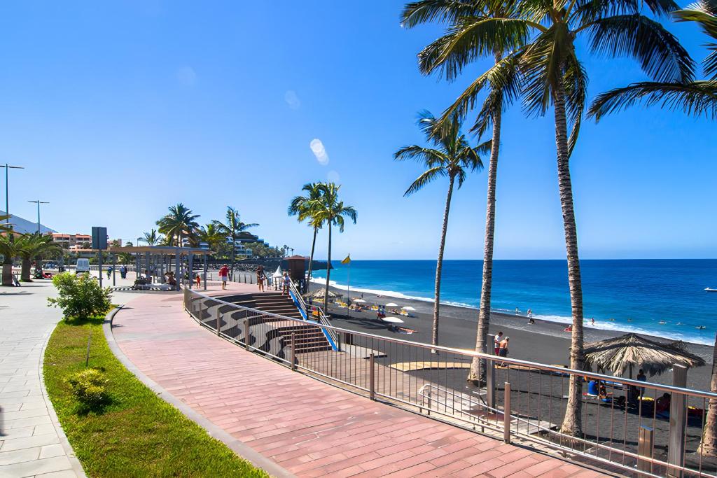 a sidewalk next to a beach with palm trees and the ocean at Naos Suite in Puerto Naos
