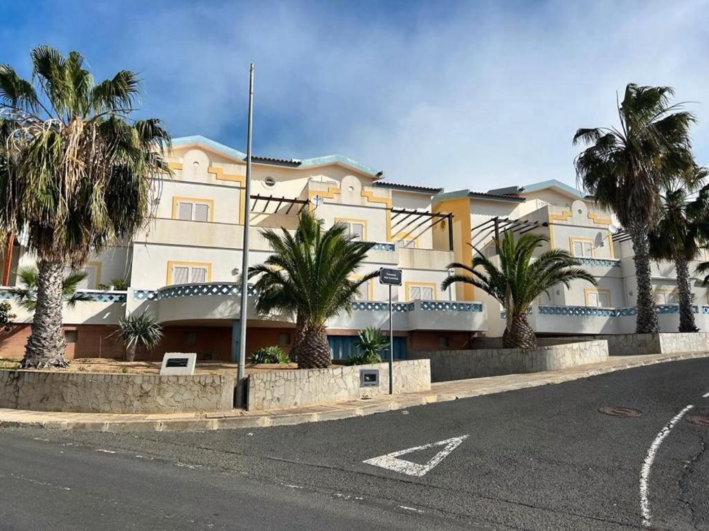 a building with palm trees in front of a street at Porto Santo Rentals in Porto Santo