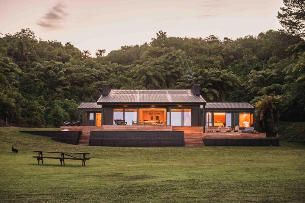 a house in the middle of a field with a bench at Lakefront Luxury at Okere Falls Lake Rotoiti in Rotorua