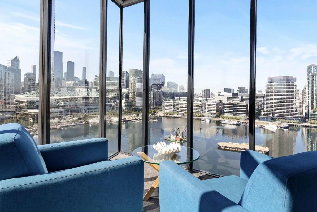 a room with blue chairs and a view of a city at Docklands Harbour View 3BR with Free Parking in Melbourne