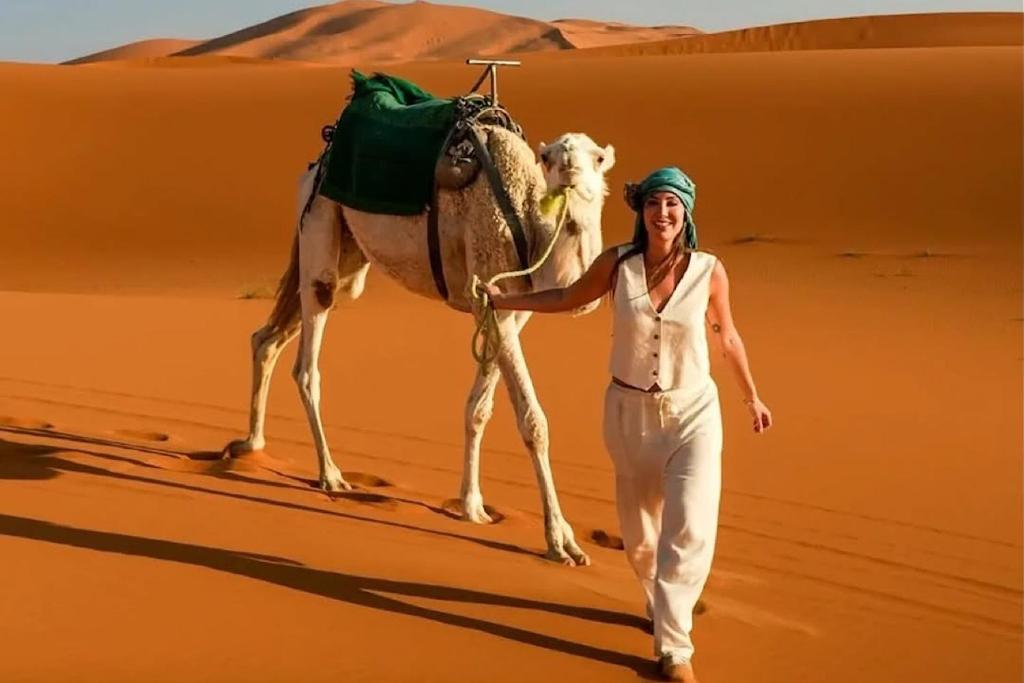 a woman walking in the desert with a camel at Stargazing Merzouga Camp in Merzouga