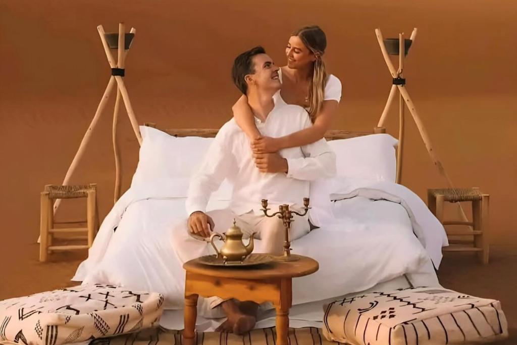 a bride and groom sitting on a bed at Merzouga Exclusive Camp in Merzouga
