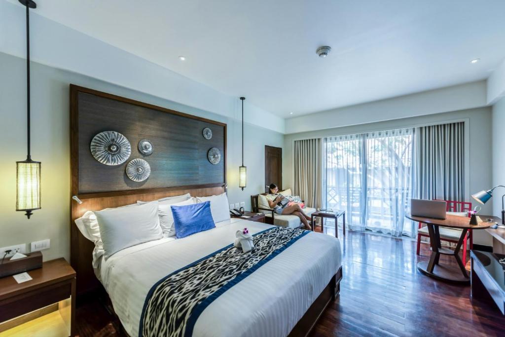 une chambre d'hôtel avec un grand lit et une femme assise sur un canapé dans l'établissement Airport Hotel King'S, à New Delhi