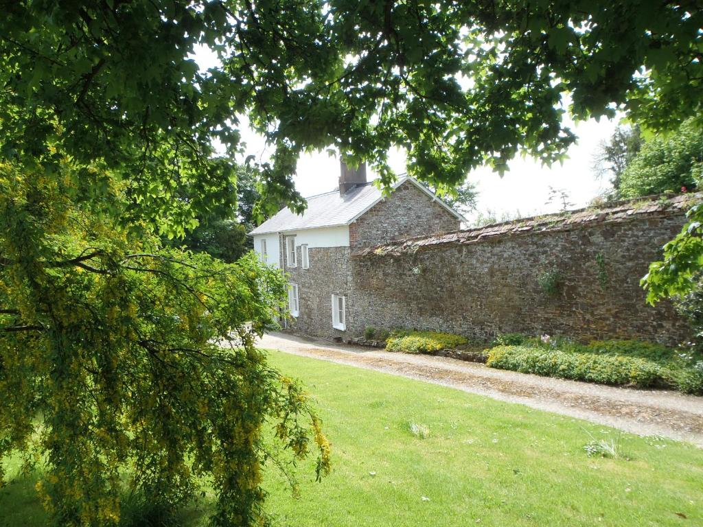 um antigo edifício de pedra com um jardim de relva ao lado de uma parede em Kipps Farm em Great Torrington