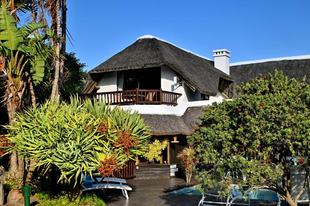 a house with a thatch roof with a deck at BonBini Guest House in St Francis Bay