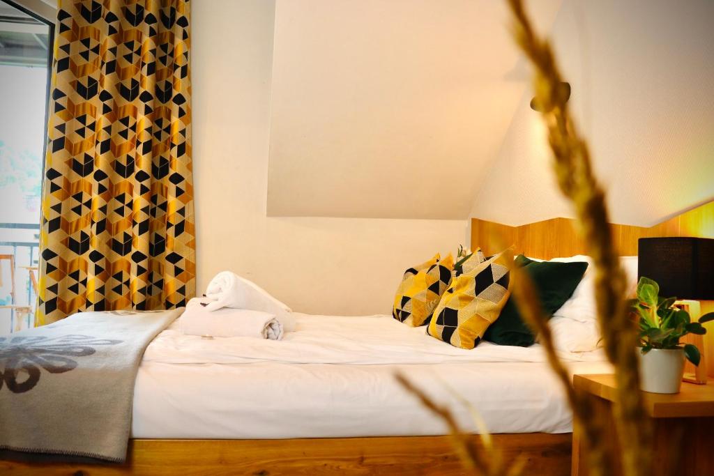 Bright bedroom with patterned yellow curtains, decorative pillows, neatly folded towels on bed.