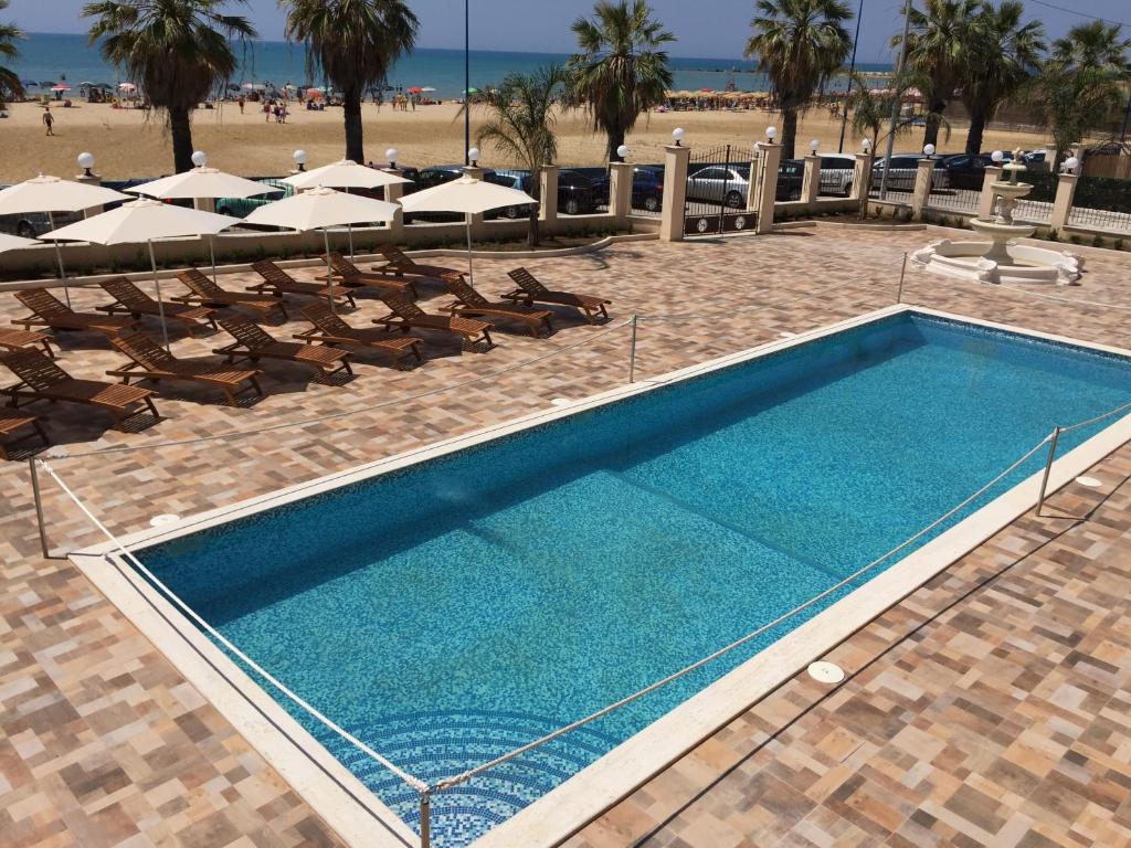 einen Pool mit Stühlen und Sonnenschirmen neben einem Strand in der Unterkunft Hotel Riviera Palace in Porto Empedocle
