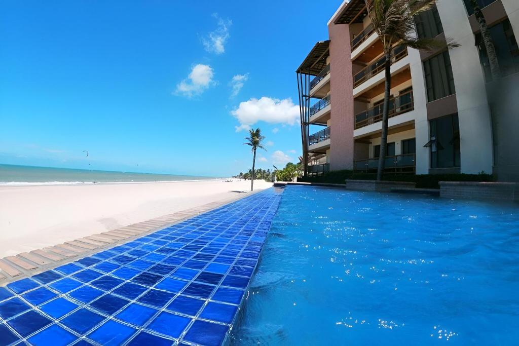 a swimming pool next to a beach next to a building at Varandas do Mar pé na areia in Cumbuco