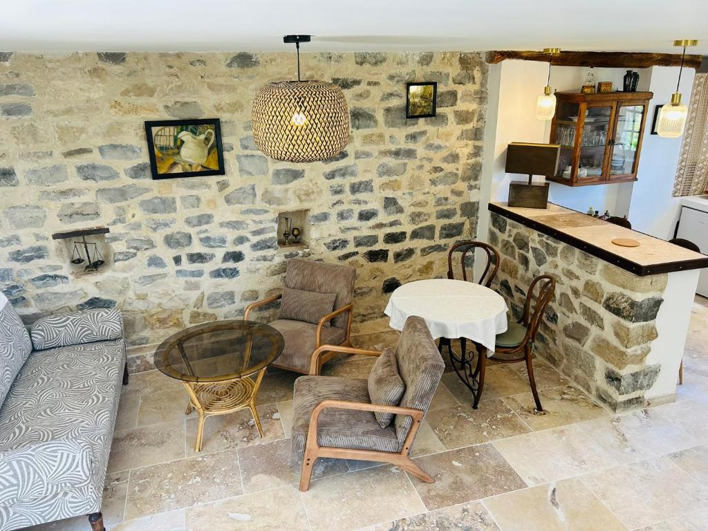 a living room with a table and chairs and a stone wall at Le Clos des Pigières Gîte le Grènetier in Vaison-la-Romaine