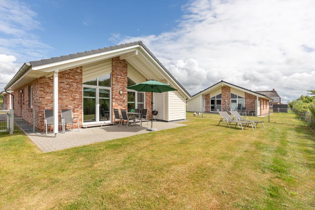 ein Haus mit einer Terrasse mit Stühlen und einem Sonnenschirm in der Unterkunft Salzwiese in Dagebüll