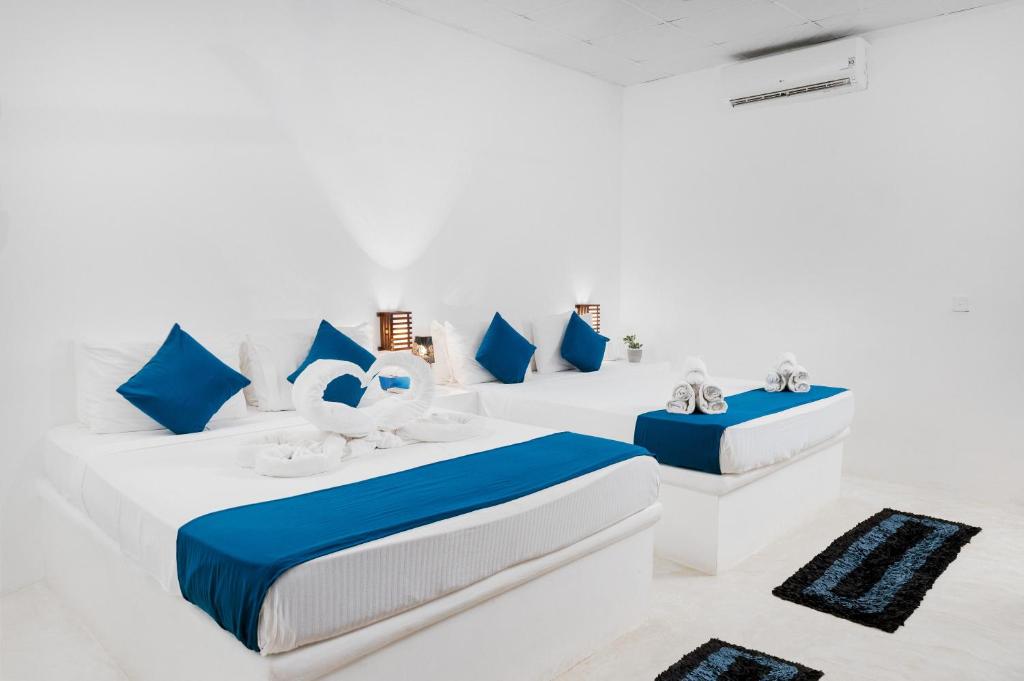 een witte kamer met drie bedden en blauwe kussens bij Roshanne Beach Resort, Kalpitiya in Kalpitiya