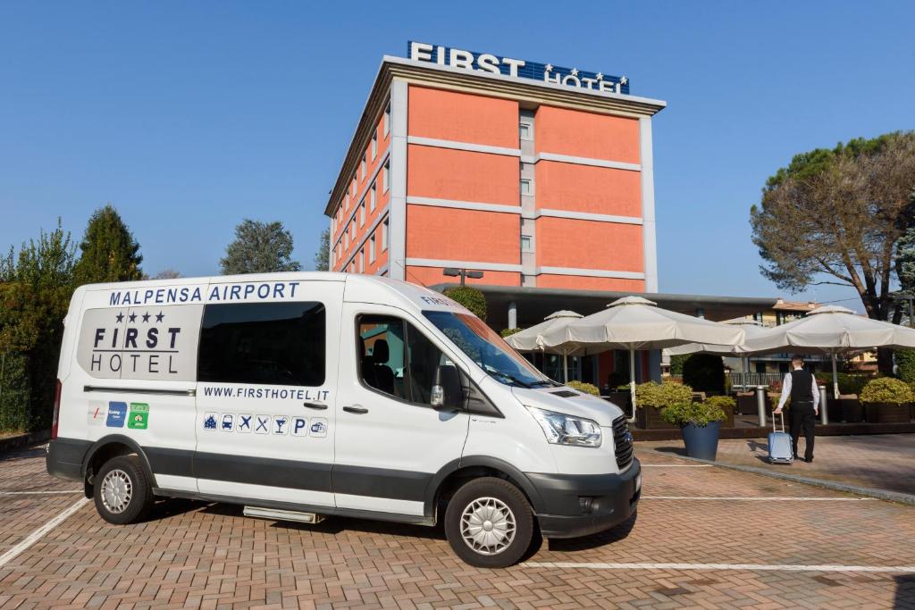
a white van parked in front of a building at First Hotel Malpensa in Case Nuove
