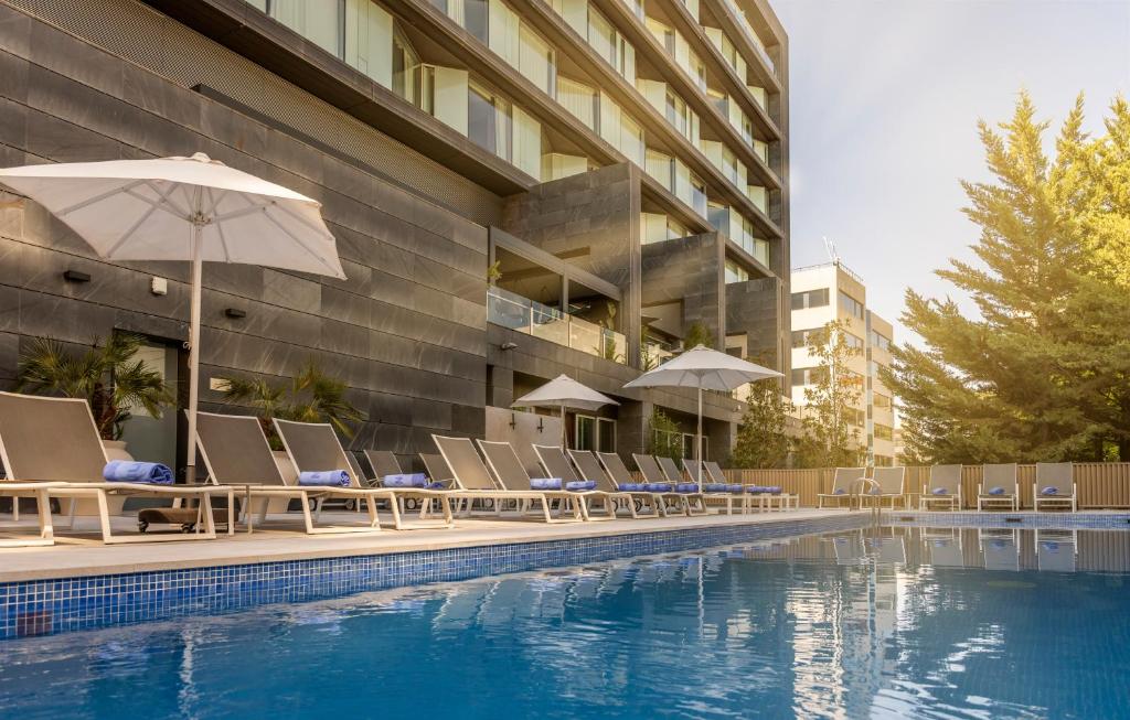 a pool with chairs and umbrellas next to a building at Ilunion Atrium in Madrid