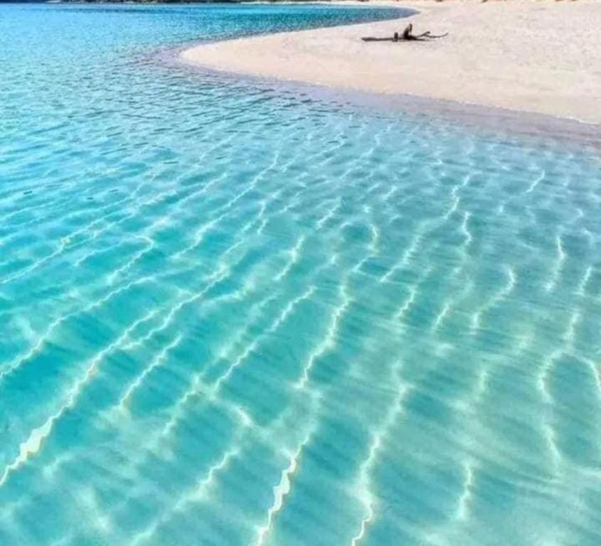 a beach with blue water and a person laying on the sand at Matrouh Marsa in Marsa Matruh