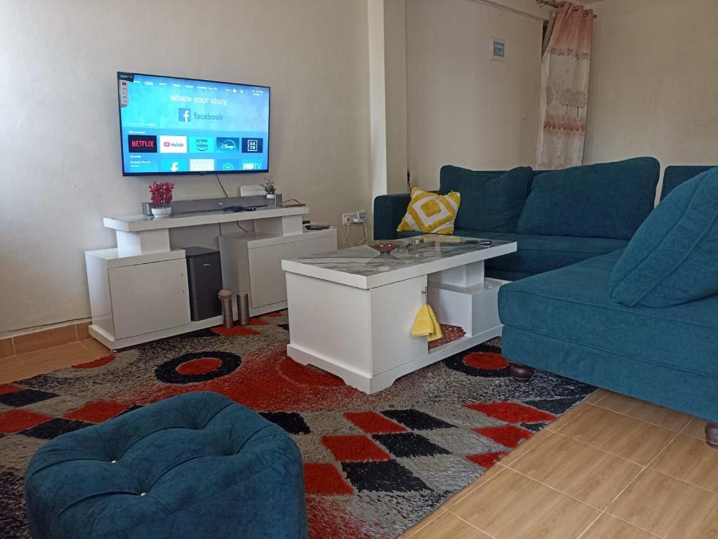 Una sala de estar con un sofá azul y un televisor en Suepower Home, en Kakamega