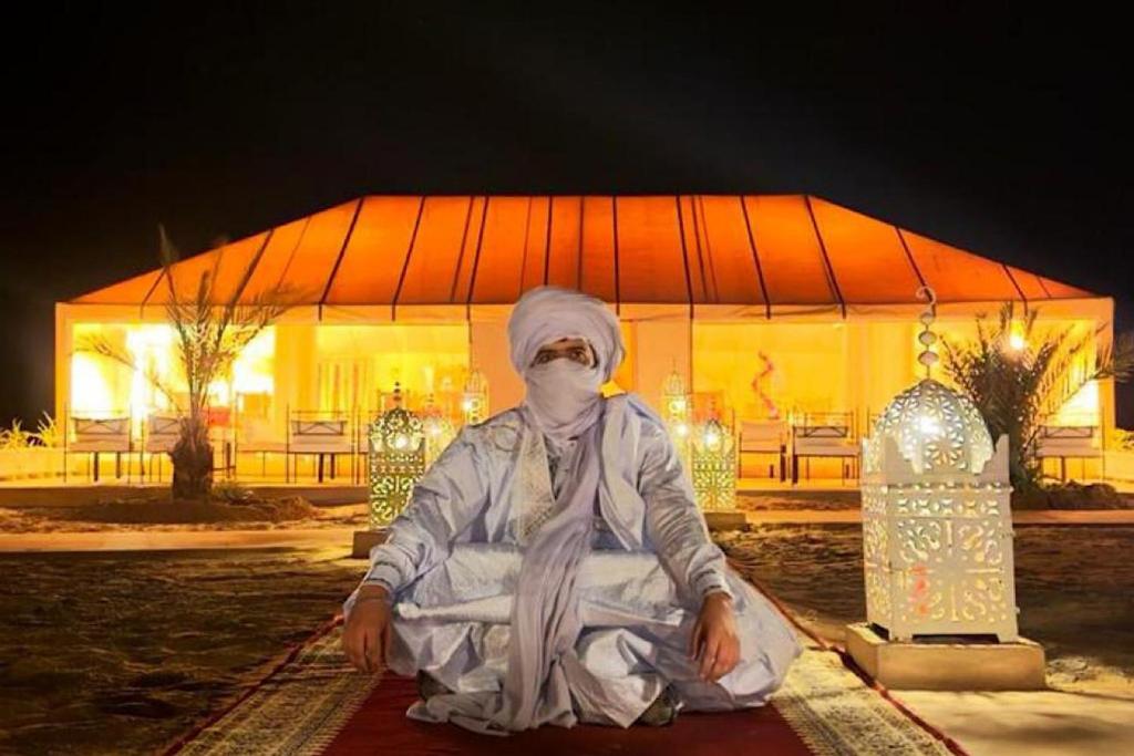 a person sitting on a rug in front of a building at Global Luxury Camp in Merzouga