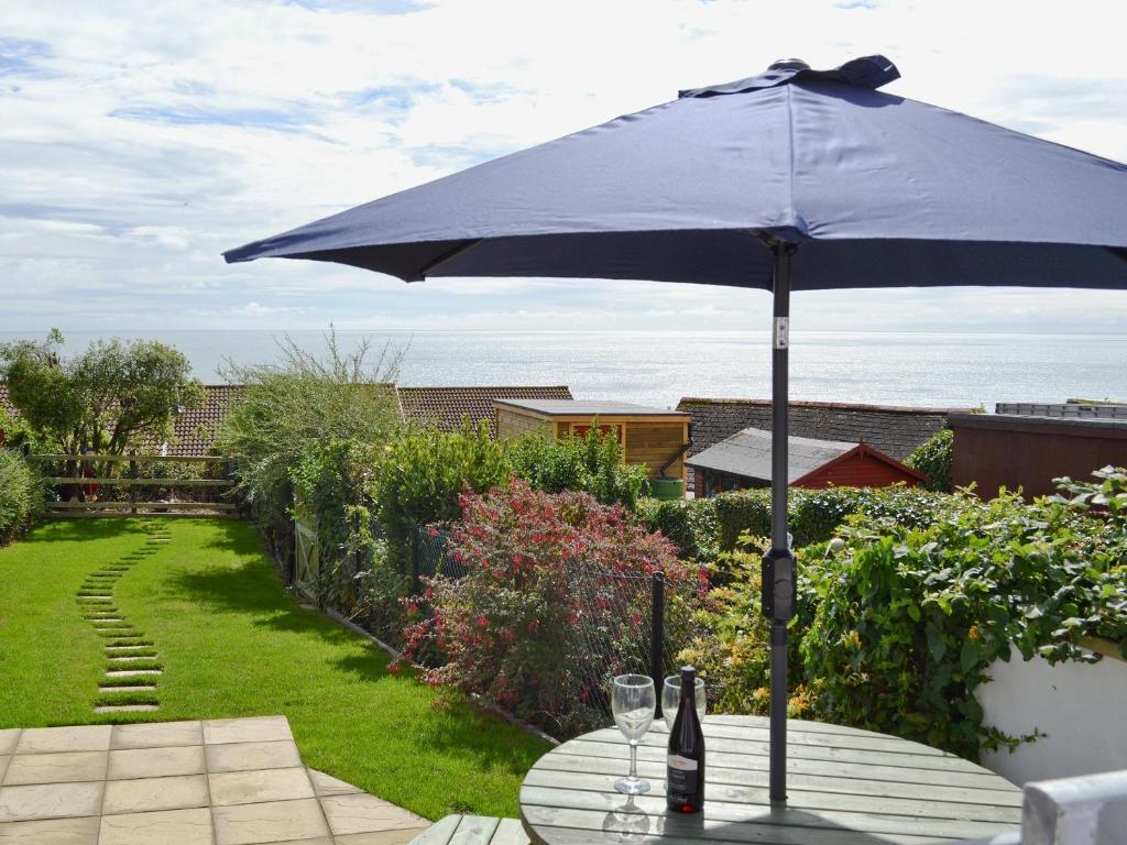 a blue umbrella on a table with a bottle and glasses at Buckingham Cottage in Ventnor