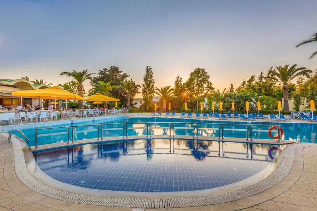 a pool at a resort with tables and chairs at Kipriotis Hippocrates Hotel in Kos