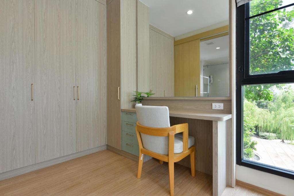 A built-in dressing desk sits beside a large wardrobe and a window overlooking dense greenery.