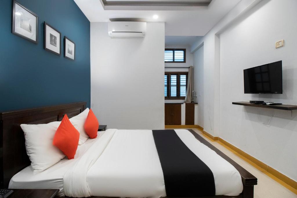 ein Schlafzimmer mit einem Bett mit orangefarbenen Kissen und einem Fernseher in der Unterkunft Collection O Victorian Comforts in Bangalore