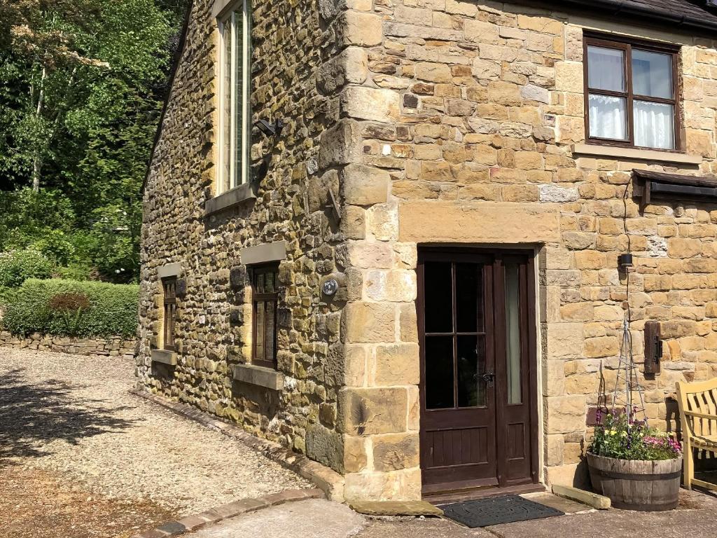 a stone building with a brown door and a bench at Calico Cottage in Hope