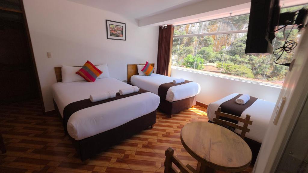 a room with three beds and a table and a window at Mapi Garden's Machupicchu in Machu Picchu