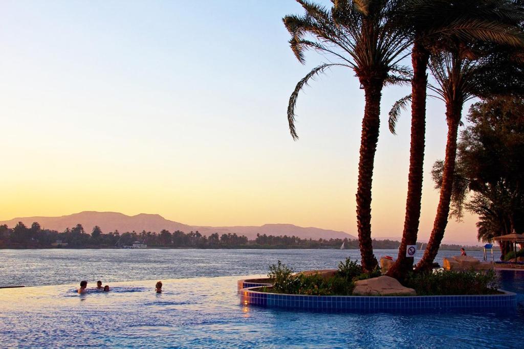 a swimming pool with palm trees and people in the water at Jolie Ville Hotel & Spa Kings Island Luxor in Luxor