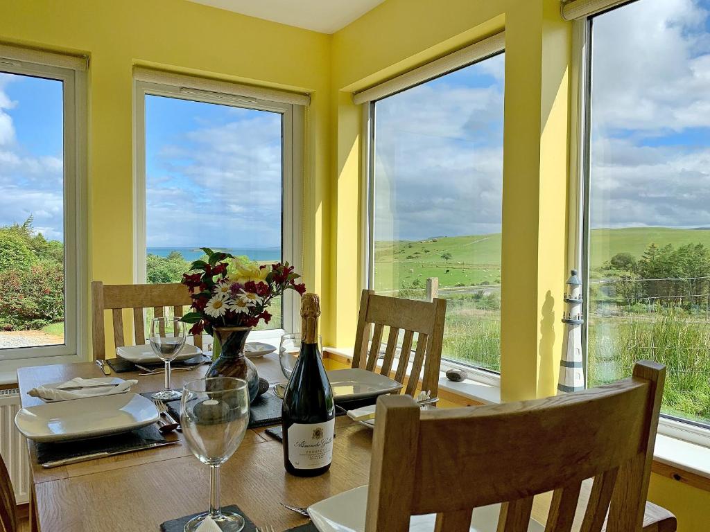 a dining room with a table with a bottle of wine at Teenys Cottage in Flashader