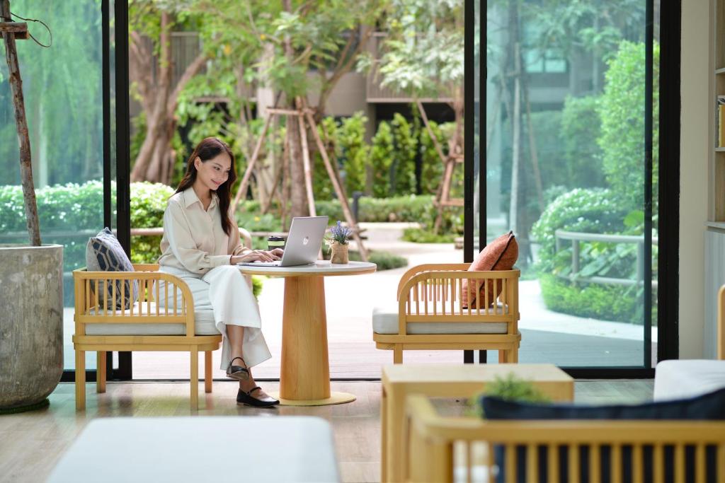 A garden-facing lounge table set up for laptop work beside floor-to-ceiling glass.