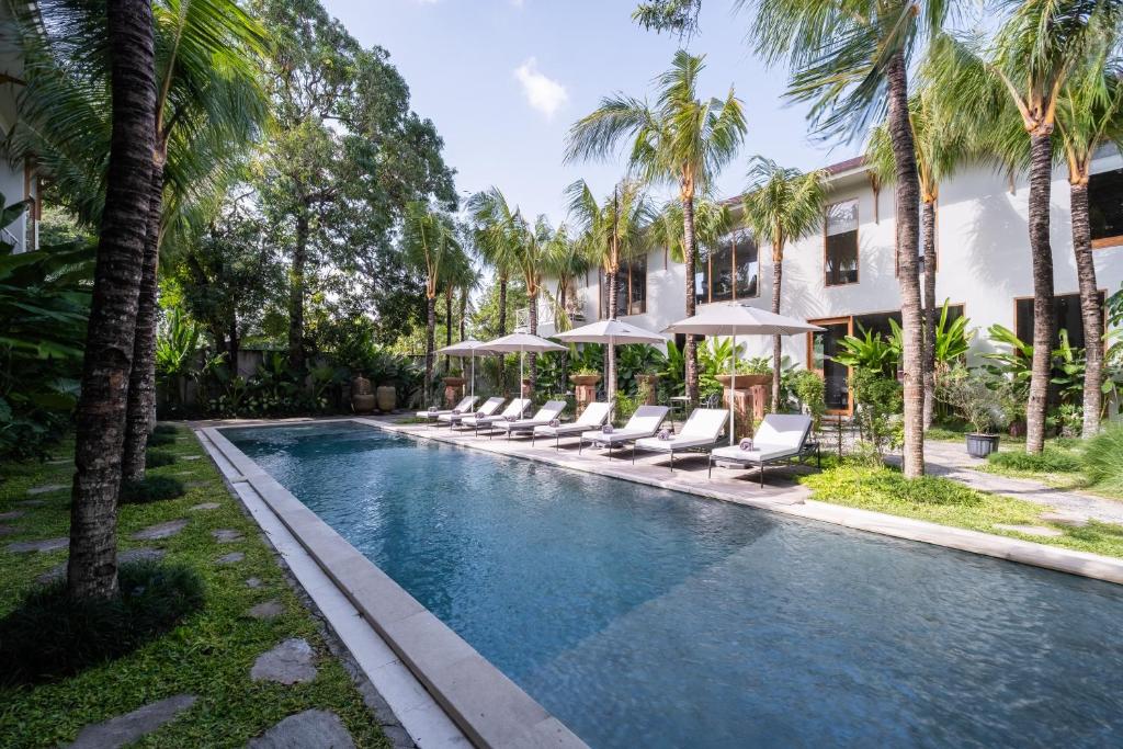 a swimming pool with lounge chairs and palm trees at Anam Tang New Rooms & Cafe near Seminyak in Seminyak