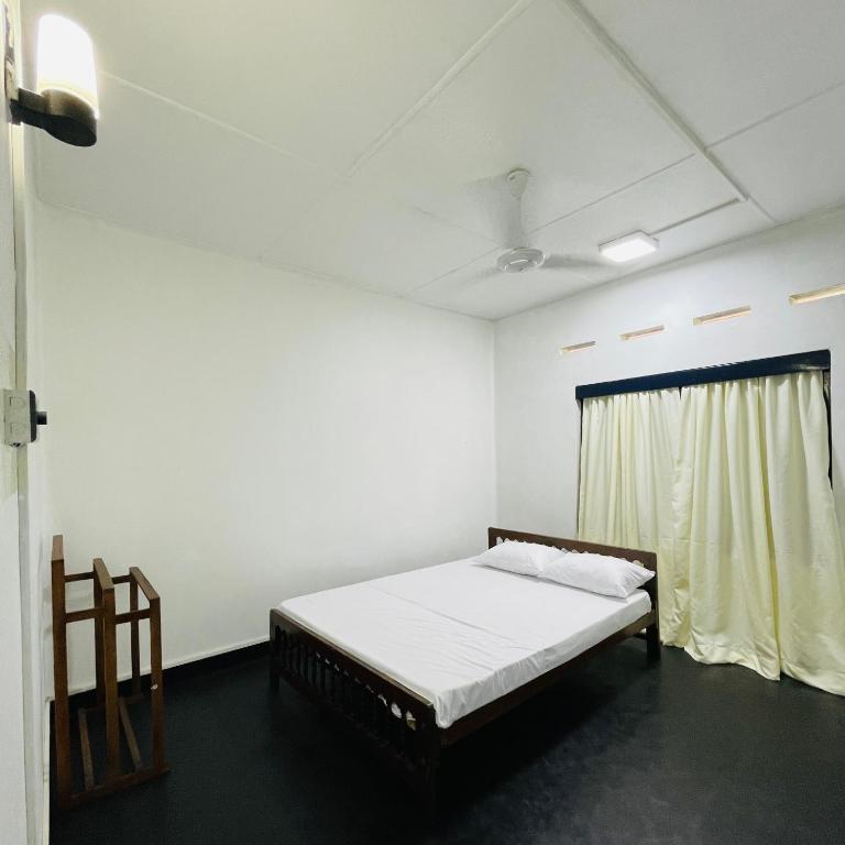 ein weißes Zimmer mit einem Bett und einem Fenster in der Unterkunft Ocean's Whisper in Paiyagala South