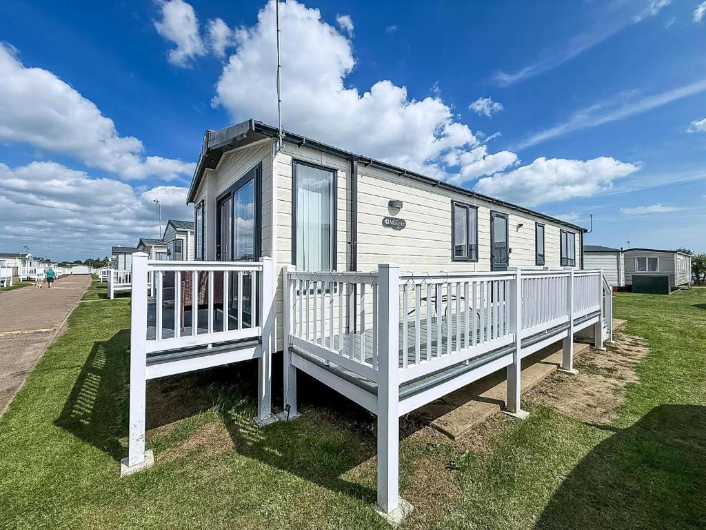 a small house with a white fence in the grass at Stunning 6 Berth Caravan, Close To The Beach In Suffolk Ref 68067Cr in Lowestoft