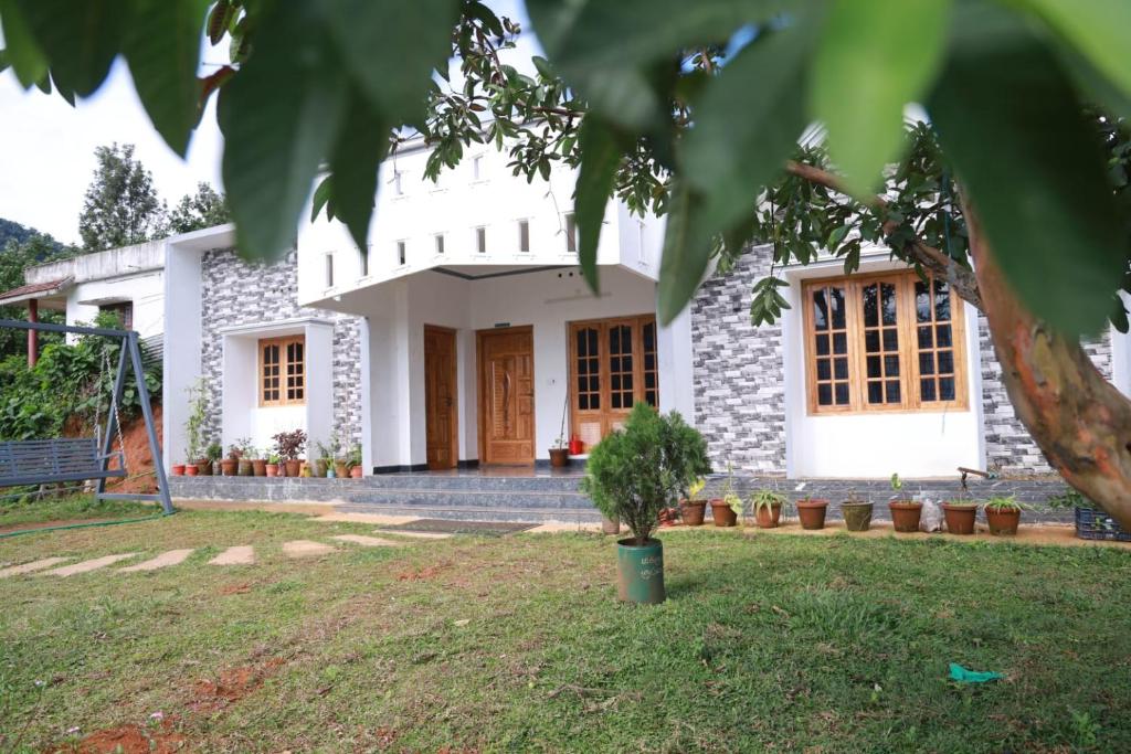 una casa blanca con un árbol delante en Munnar Mountain view cottage, en Munnar