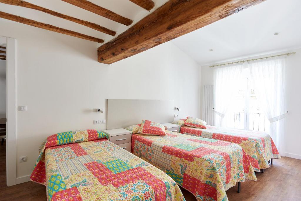 two beds in a room with white walls and wooden ceilings at Balcon del Encierro in Pamplona
