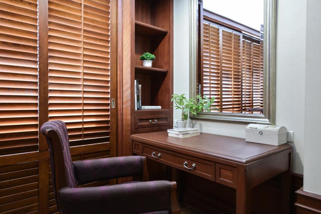A compact wooden writing desk set beside shuttered windows.