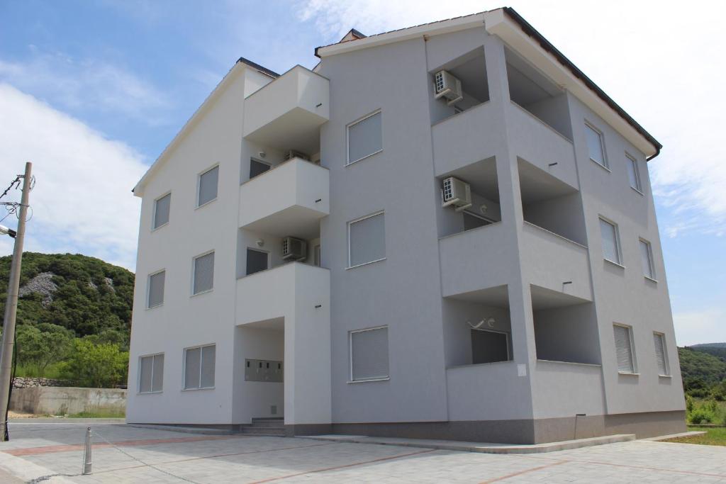 a white building with balconies in a parking lot at Apartments PETRUSIC in Rab