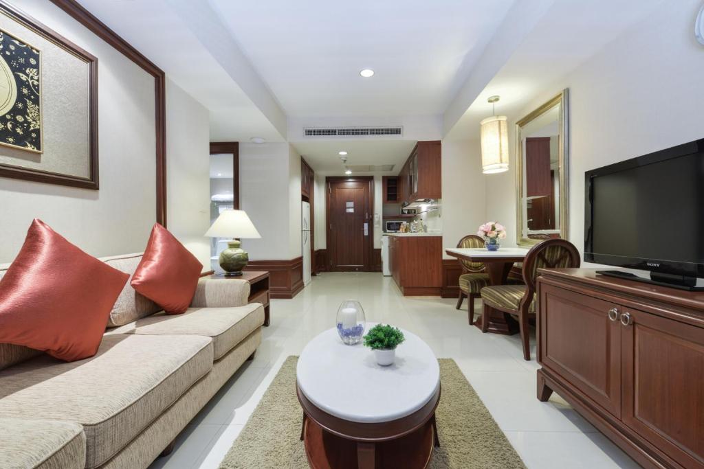 A furnished living area with a sofa, television, dining table and kitchenette beyond.
