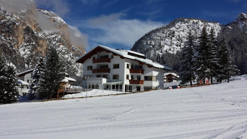 a building on a snow covered hill with a mountain at Residence Villa Funtanes in Selva di Val Gardena