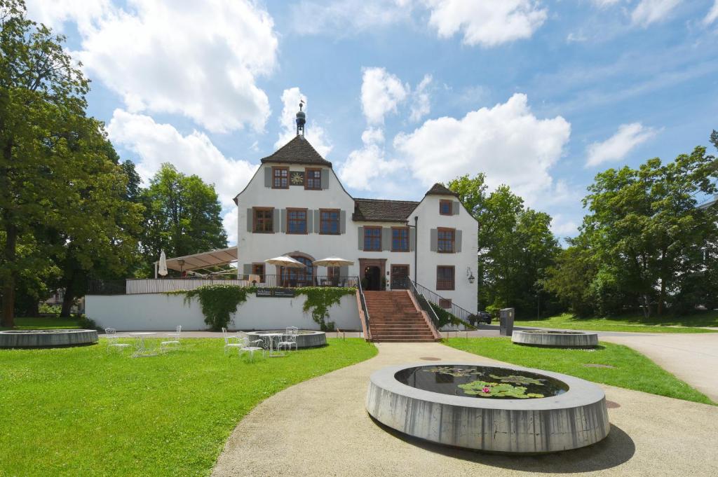 Une grande maison blanche avec une fontaine en face de celle-ci dans l'établissement Hotel im Schlosspark, à Bâle